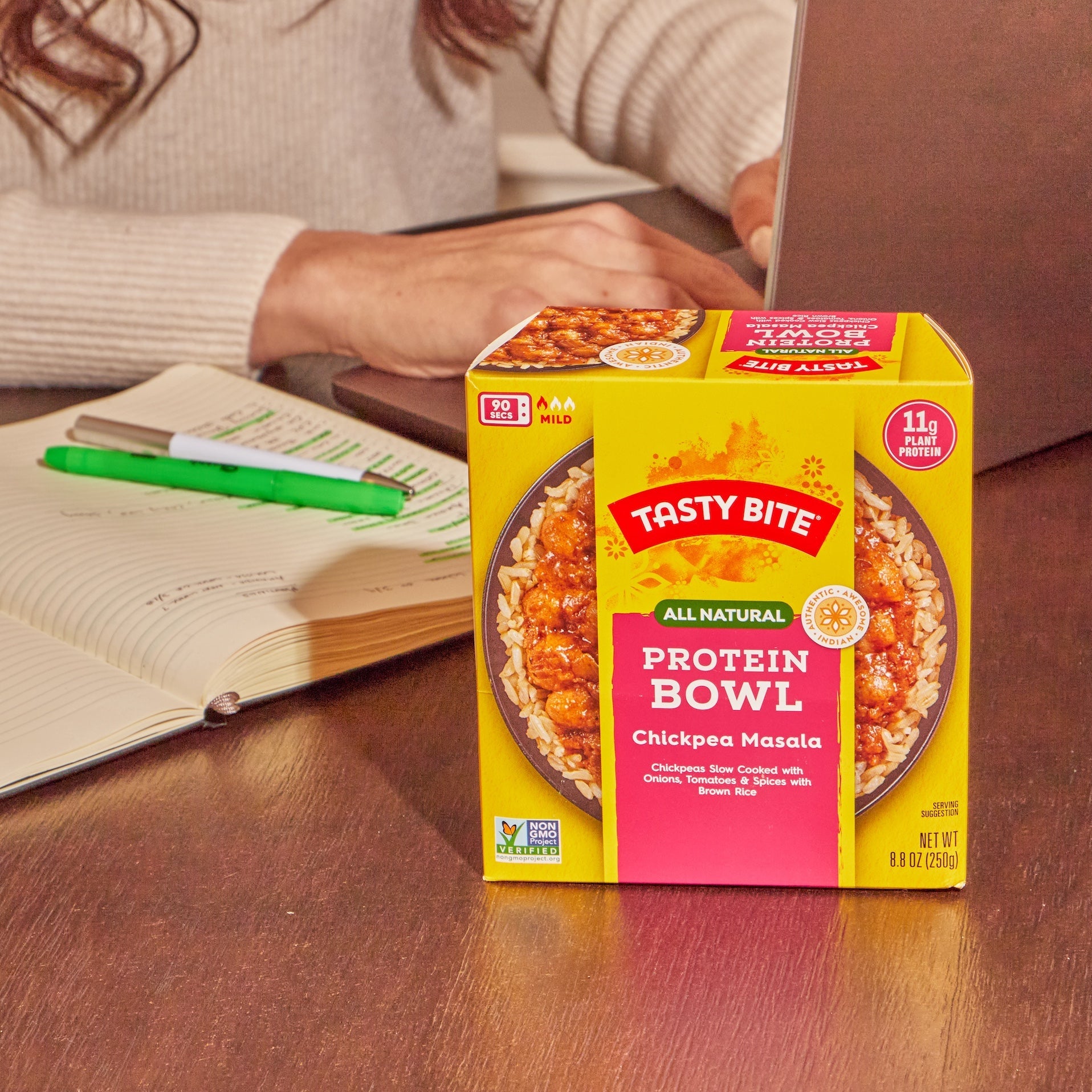 Tasty Bite Protein Bowl Chickpea Masala ready meal on a desk with notebook and laptop, perfect for a quick work lunch