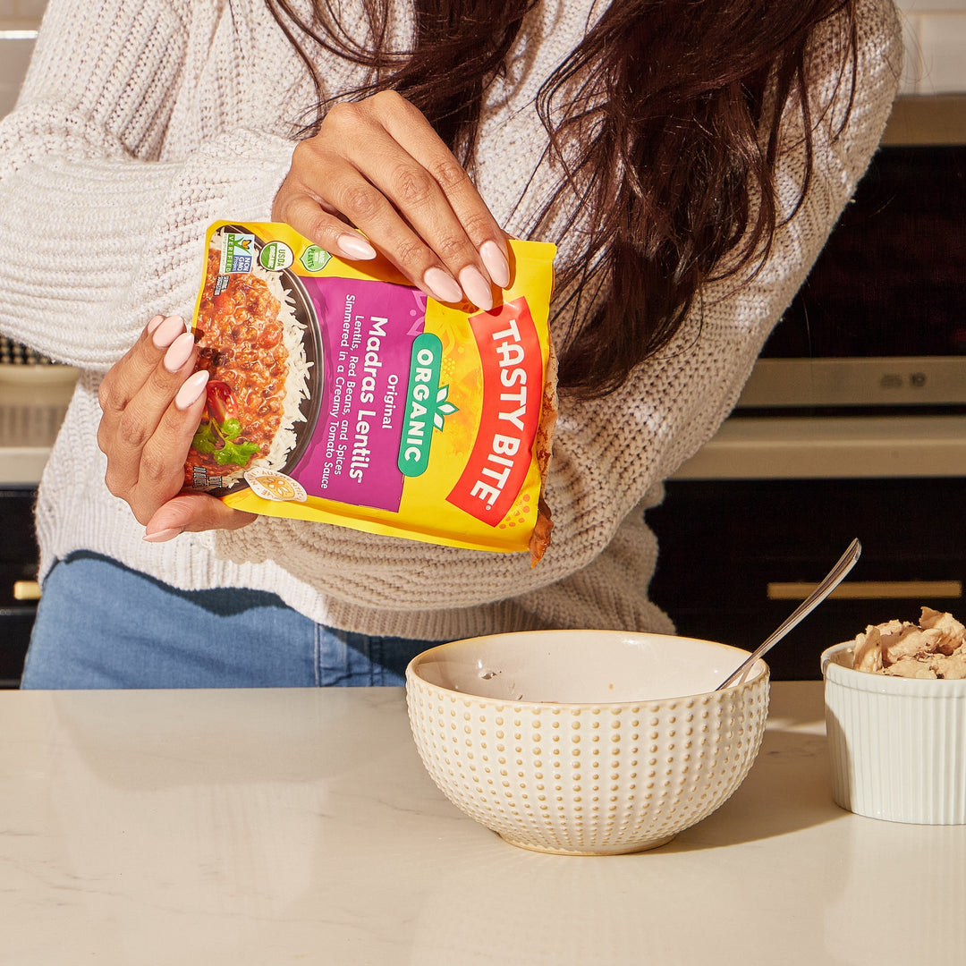 Woman pouring Tasty Bite Organic Madras Lentils into a bowl for a quick and easy ready-to-eat meal